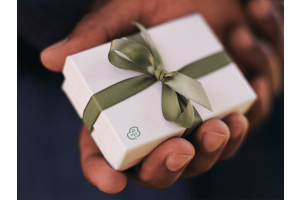 A hand holding a white gift box with a greenribbon and Greenfibres logo