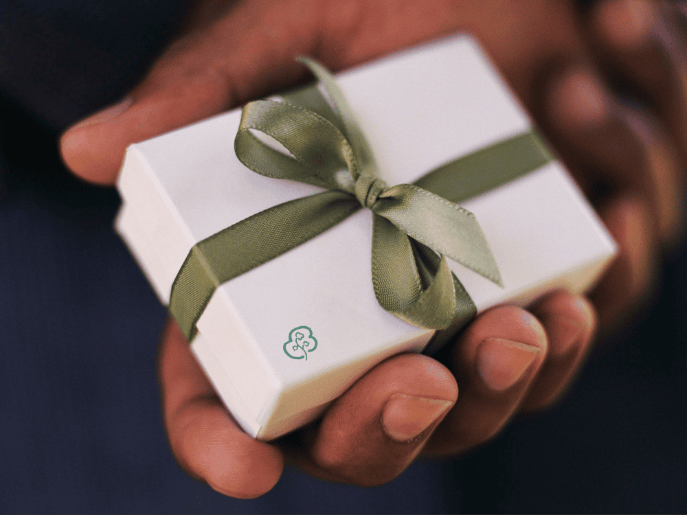 A hand holding a white gift box with a greenribbon and Greenfibres logo