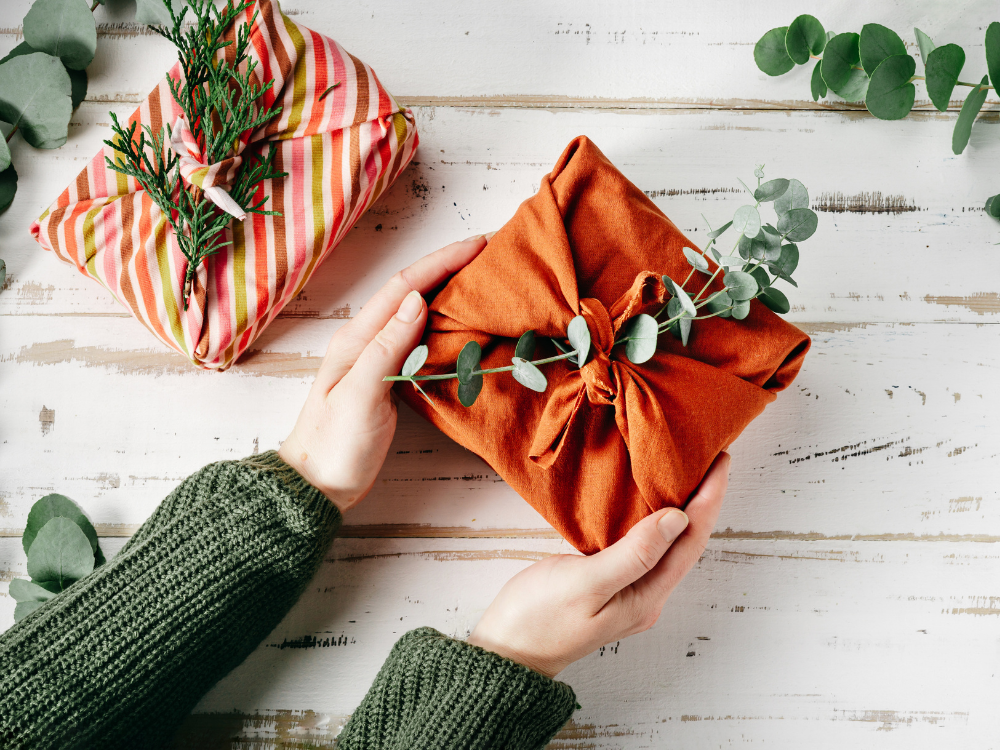 Hands offering a gift wrapped in organic fabric