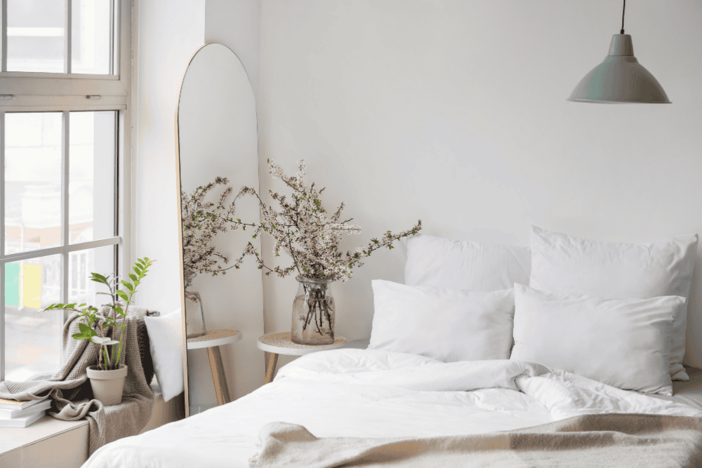 a bed with the covers pulled back in front of a white wall next to a large window with indoor plants 